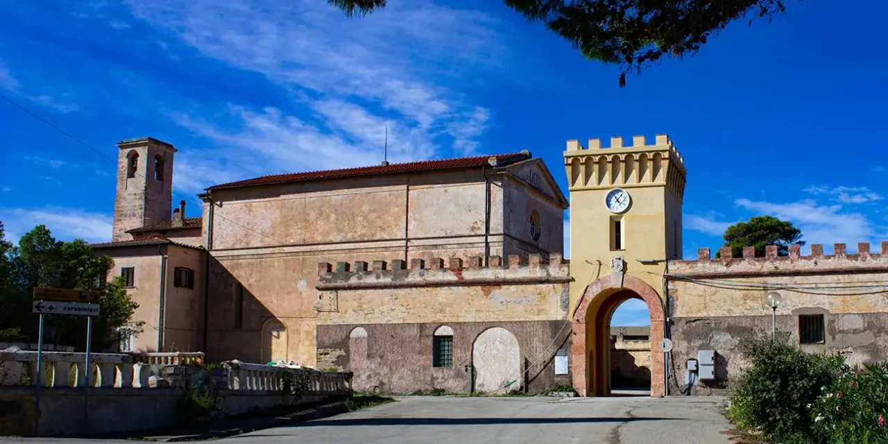 Antico borgo sull'isola di Pianosa, con torre dell'orologio e campanile sotto un cielo azzurro.
