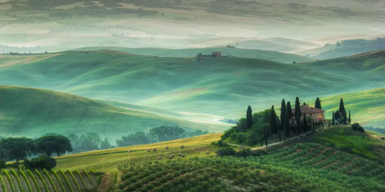 Dolci colline verdi del Val d'Orcia, con una casa colonica in cima a una collina e cipressi. Un paesaggio da cartolina, uno dei tanti punti panoramici mozzafiato.
