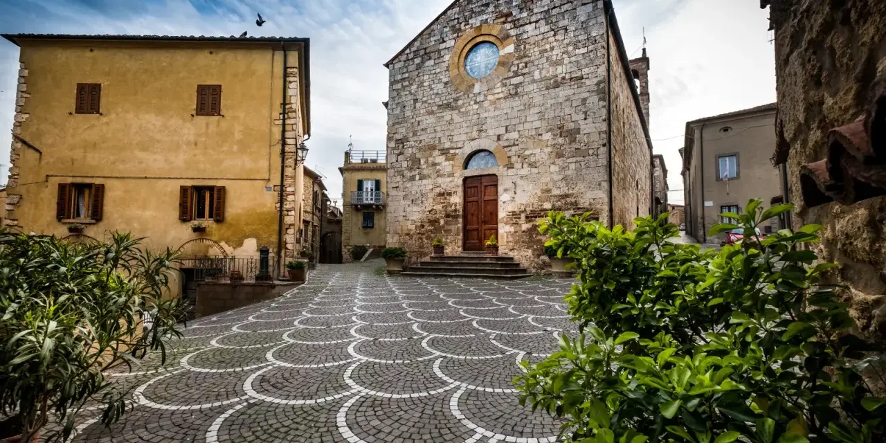 Piazza di Bibbona, cosa vedere: chiesa in pietra con rosone, case gialle e pavimentazione a ventaglio.