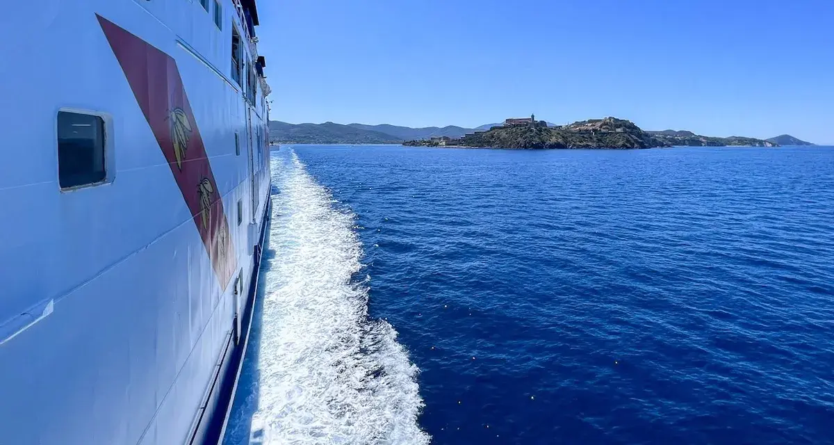 Traghetto in navigazione verso l'isola d'Elba, con la costa all'orizzonte sotto un cielo azzurro.