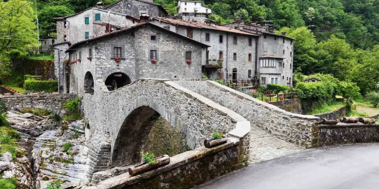 Ponte in pietra a Vergemoli, con case in pietra e vegetazione lussureggiante sullo sfondo. Le antiche fabbriche di Vergemoli sembrano emergere dalla collina.
