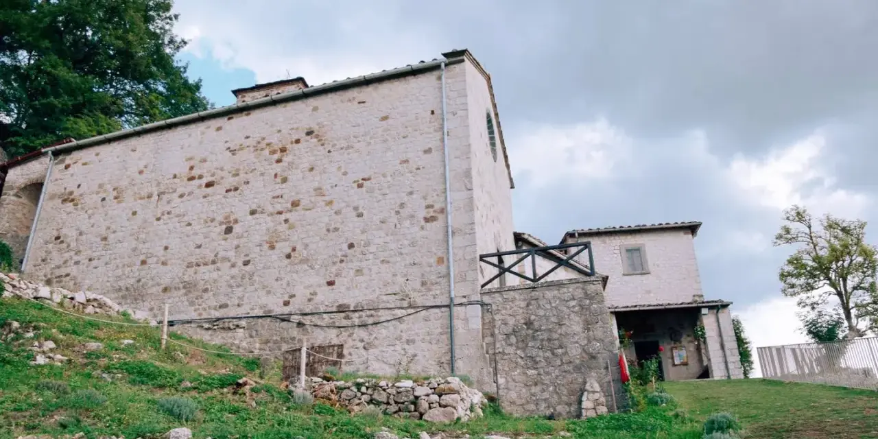 Antico eremo di Cerbaiolo, con muri in pietra grezza e vegetazione rigogliosa che sale sul pendio.
