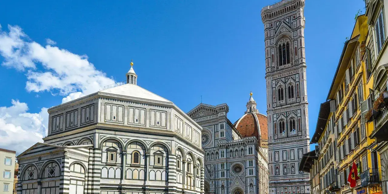 La piazza del Duomo a Firenze con il Battistero, il Campanile di Giotto e la cupola del Brunelleschi sotto un cielo azzurro.