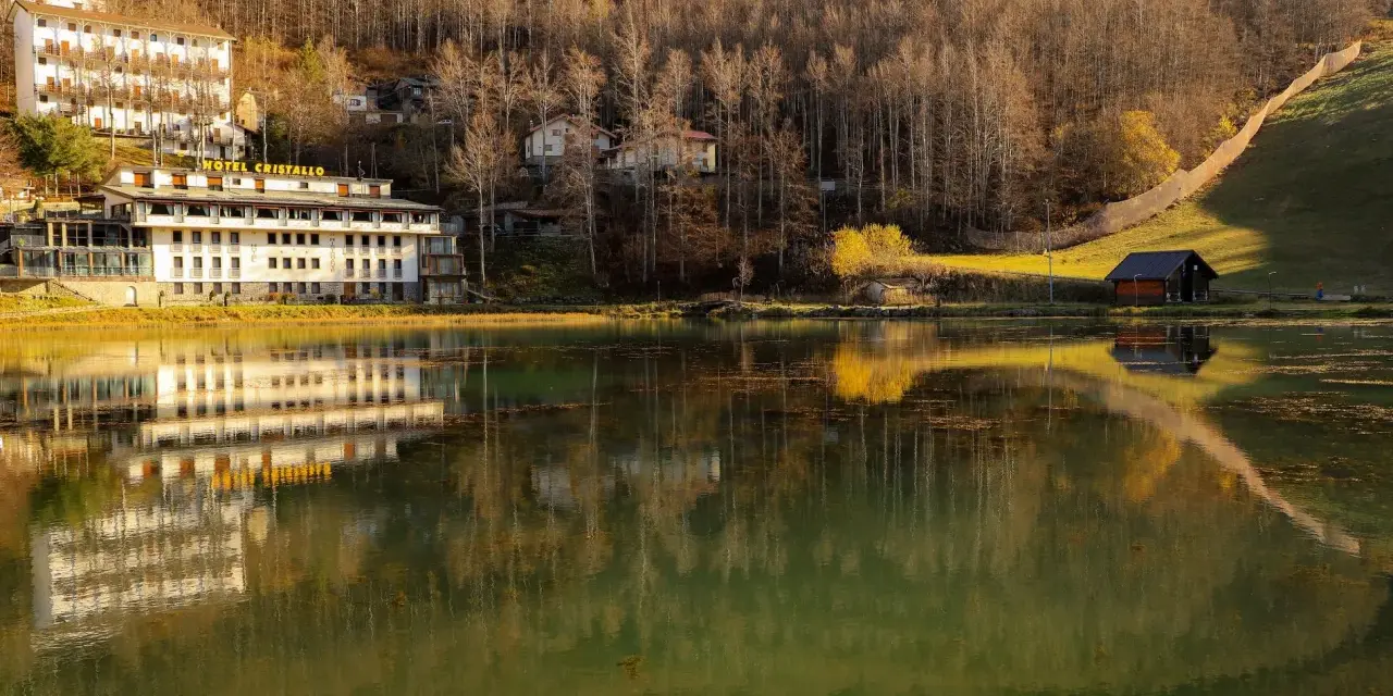 Hotel Cristallo sul Passo del Cerreto, riflesso sull'acqua calma di un lago circondato da boschi autunnali.