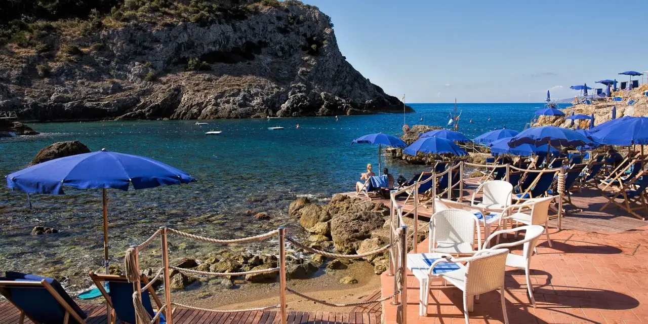 Le argentario spiagge più belle, con ombrelloni blu e lettini su una terrazza in legno, affacciate sul mare cristallino.
