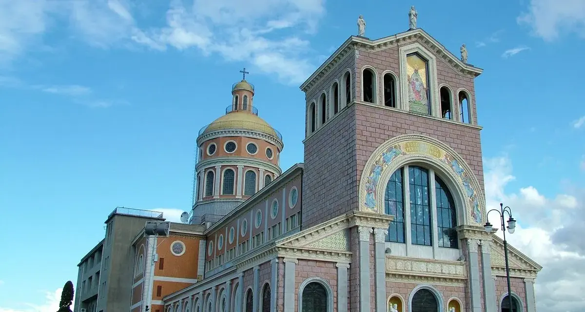 Imponente Santuario di Tindari con cupola dorata e facciata decorata, sotto un cielo azzurro con nuvole bianche.