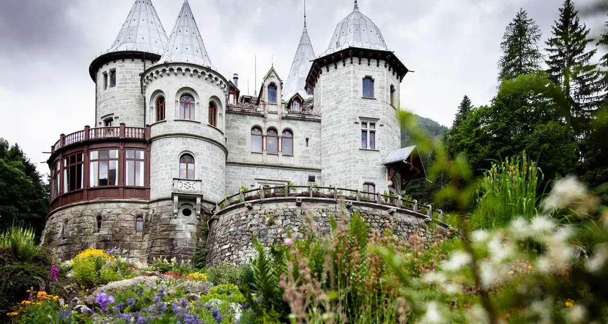 Un fiabesco castello in pietra, tra i castelli Val d'Aosta, circondato da un giardino fiorito e boschi rigogliosi.