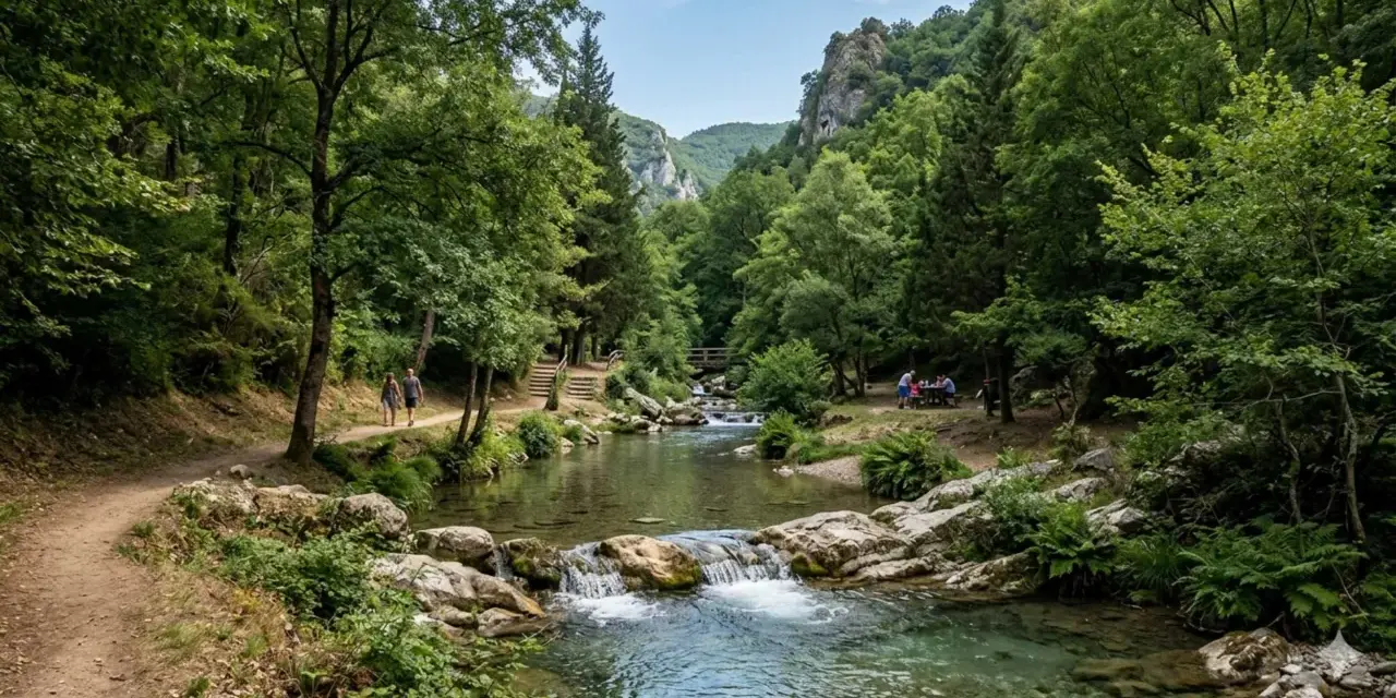 Sentiero in un bosco lussureggiante, con un fiume cristallino e una cascata. Coppia passeggia, un gruppo fa picnic. Un assaggio dei **parchi naturali Campania**.