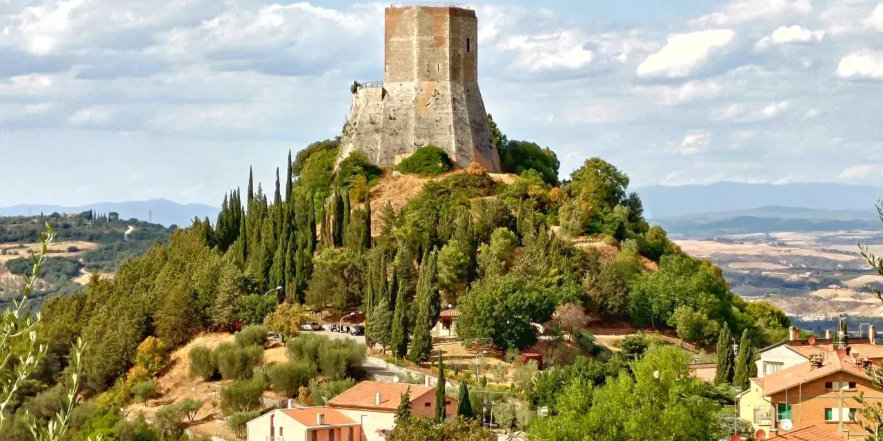 La rocca di Tentennano domina la collina, circondata da cipressi e ulivi. Sotto, un borgo con tetti rossi si adagia nel paesaggio toscano.