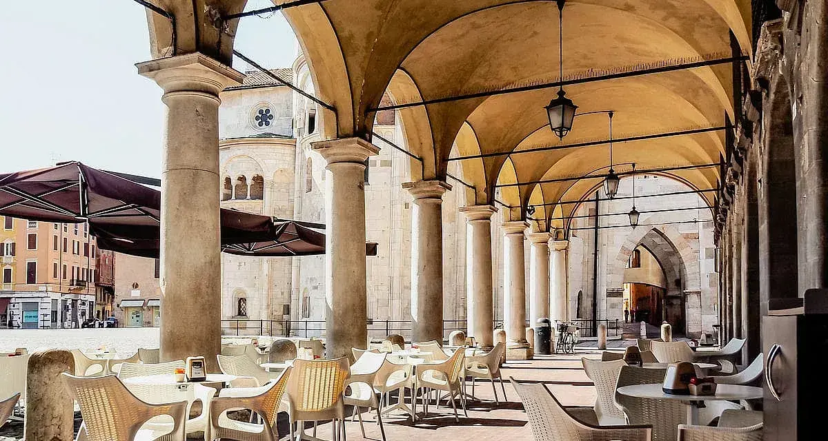 Tavolini all'aperto sotto un portico con vista sul Duomo. Un'idea su cosa fare a Modena: godersi un caffè in piazza.