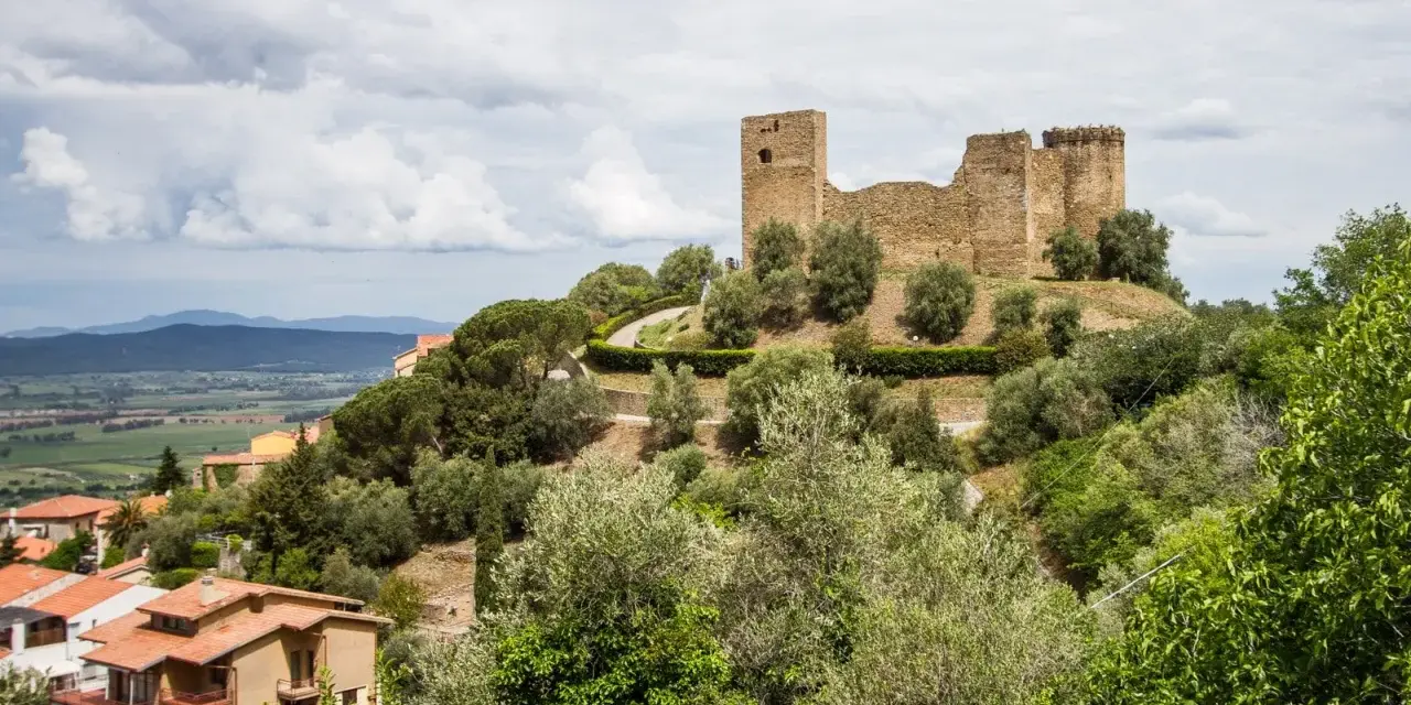 Rovine di un castello dominano il **Scarlino centro storico**, circondato da ulivi e case con tetti rossi.