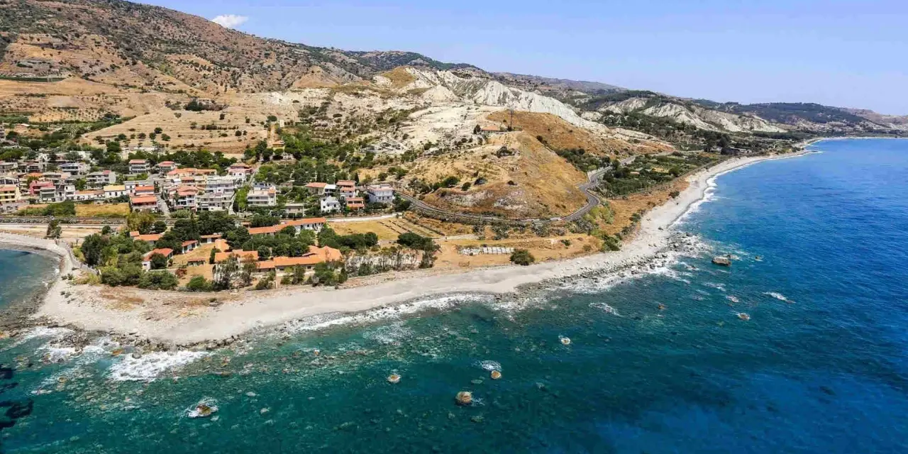 Paesaggio mozzafiato sulla costa ionica Calabria: case con tetti rossi, spiaggia rocciosa e mare blu intenso.