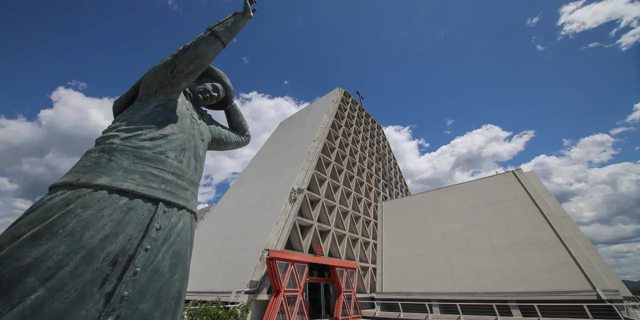 Statua bronzea davanti al Santuario Monte Grisa, con il suo ingresso rosso e la facciata a triangoli.