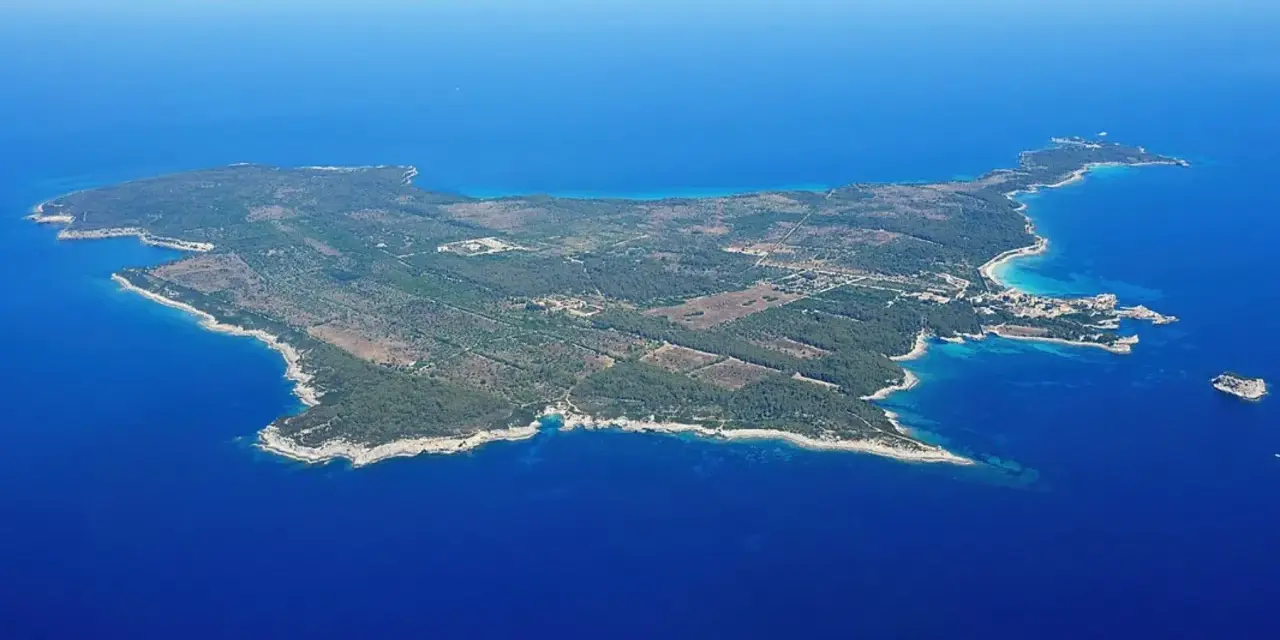 Vista aerea di un'isola verdeggiante, un'isola vicino all'Elba, con acque blu intenso e una piccola isola rocciosa in lontananza.