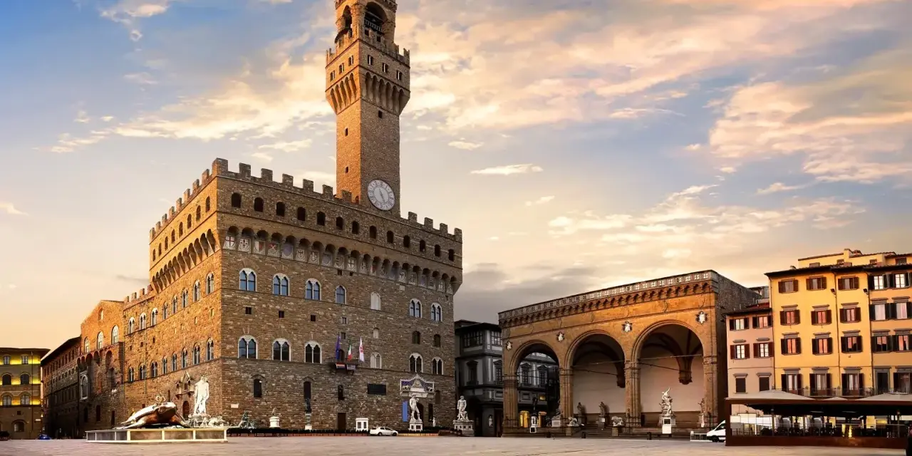 Il maestoso Palazzo Vecchio domina Piazza della Signoria, con la sua torre imponente che svetta sotto un cielo al tramonto.