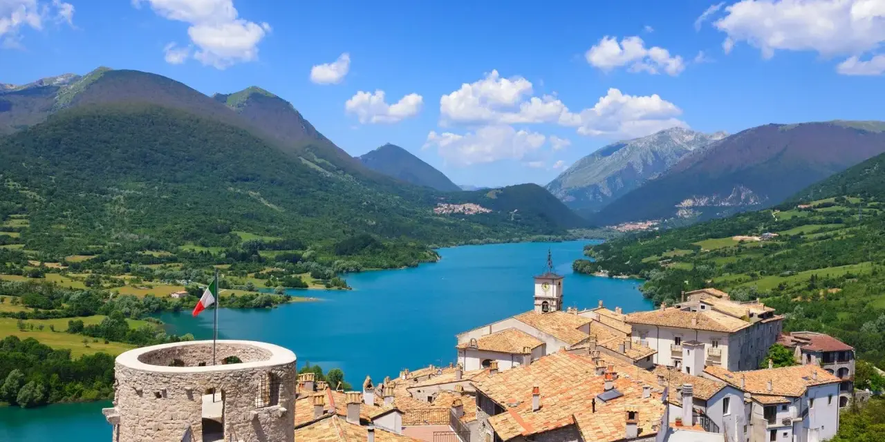 Villetta Barrea: cosa vedere? Un borgo con torre medievale, tetti rossi e un lago azzurro circondato da montagne verdi.