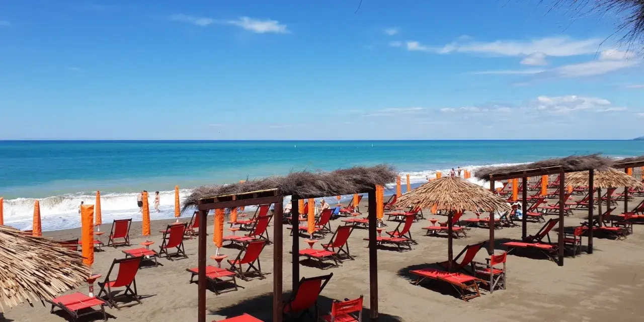 Spiaggia attrezzata a Marina di Bibbona, con lettini rossi, ombrelloni di paglia e il mare azzurro all'orizzonte.