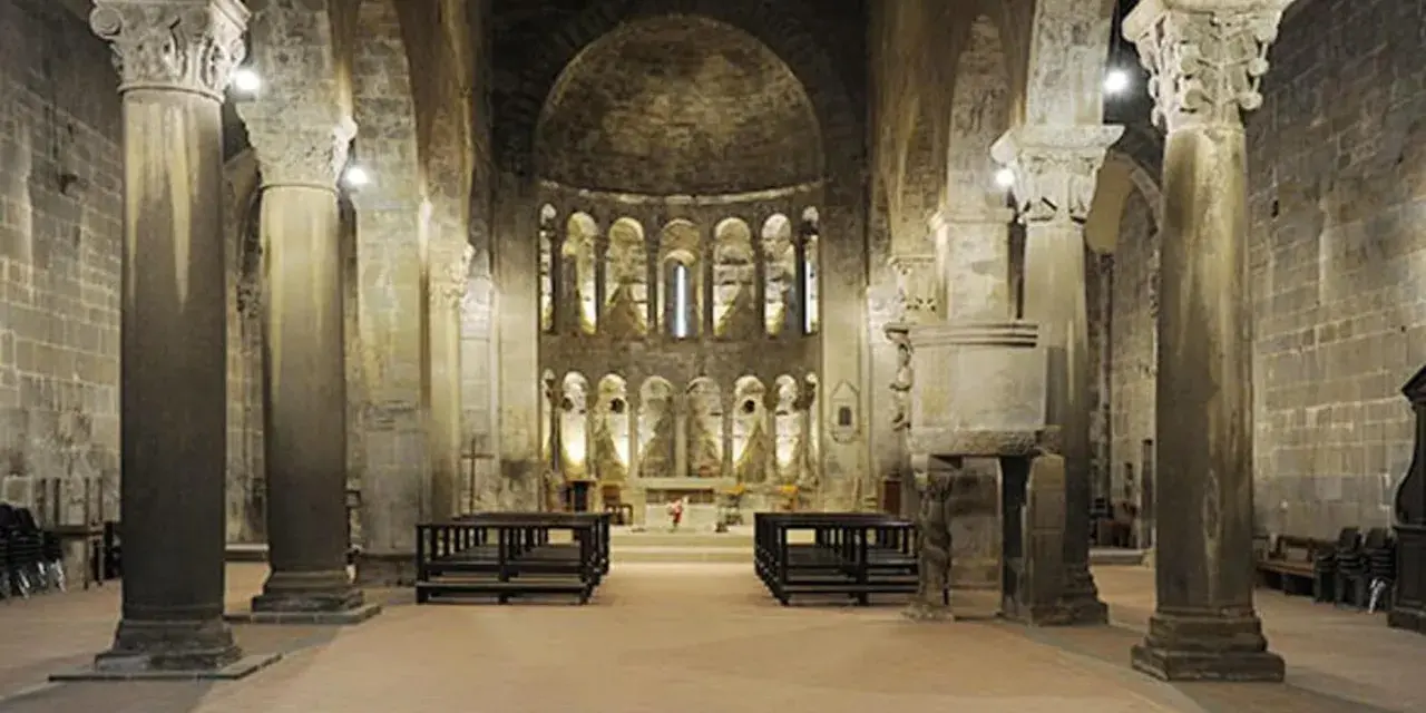 Interno della pieve di Gropina, con imponenti colonne, archi e un'abside decorata.
