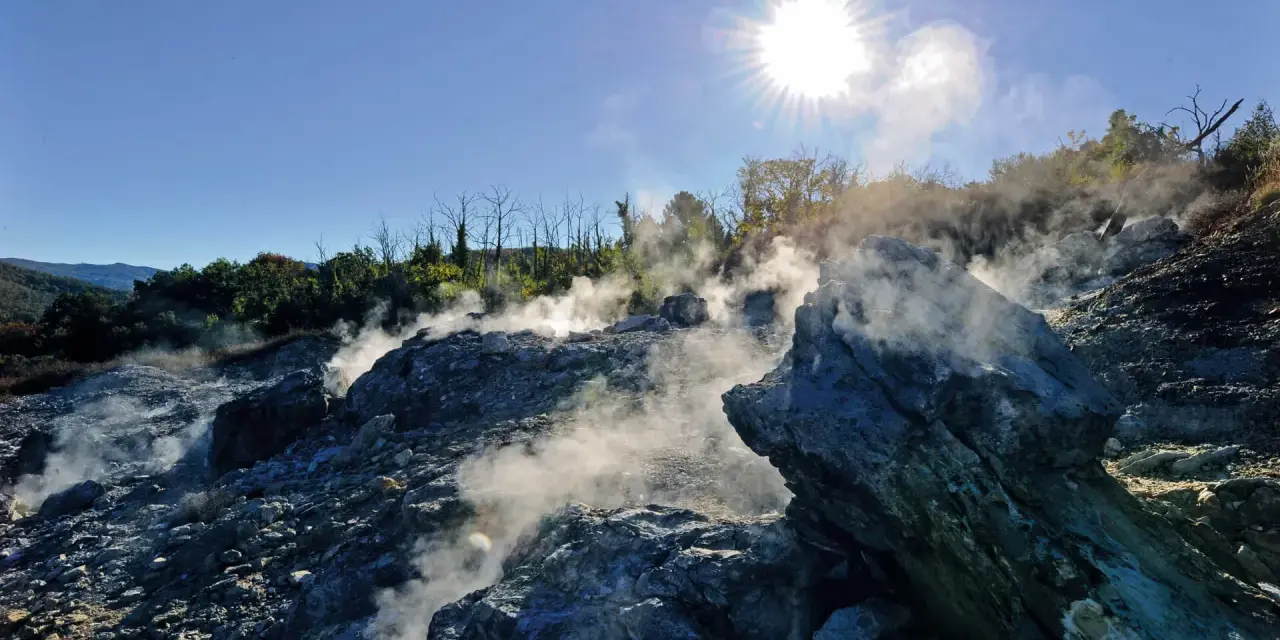 Fumarole attive nel **Val di Cecina**, con vapore che sale tra le rocce sotto un sole splendente.