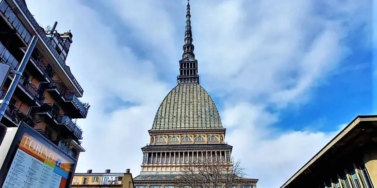 La Mole Antonelliana svetta maestosa nel cielo azzurro di Torino, circondata da edifici moderni e storici.