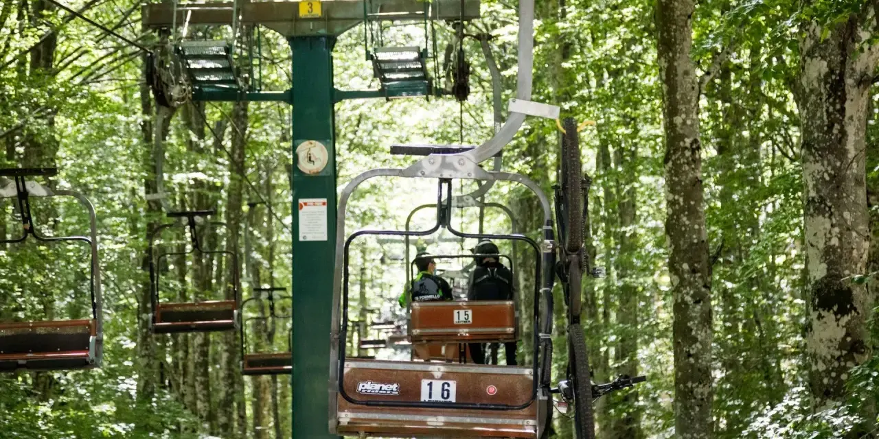 La funivia Monte Amiata trasporta due persone e una mountain bike tra gli alberi rigogliosi.