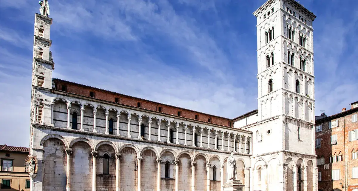 La piazza San Michele a Lucca, con la sua chiesa romanica e la torre campanaria imponente, sotto un cielo azzurro.