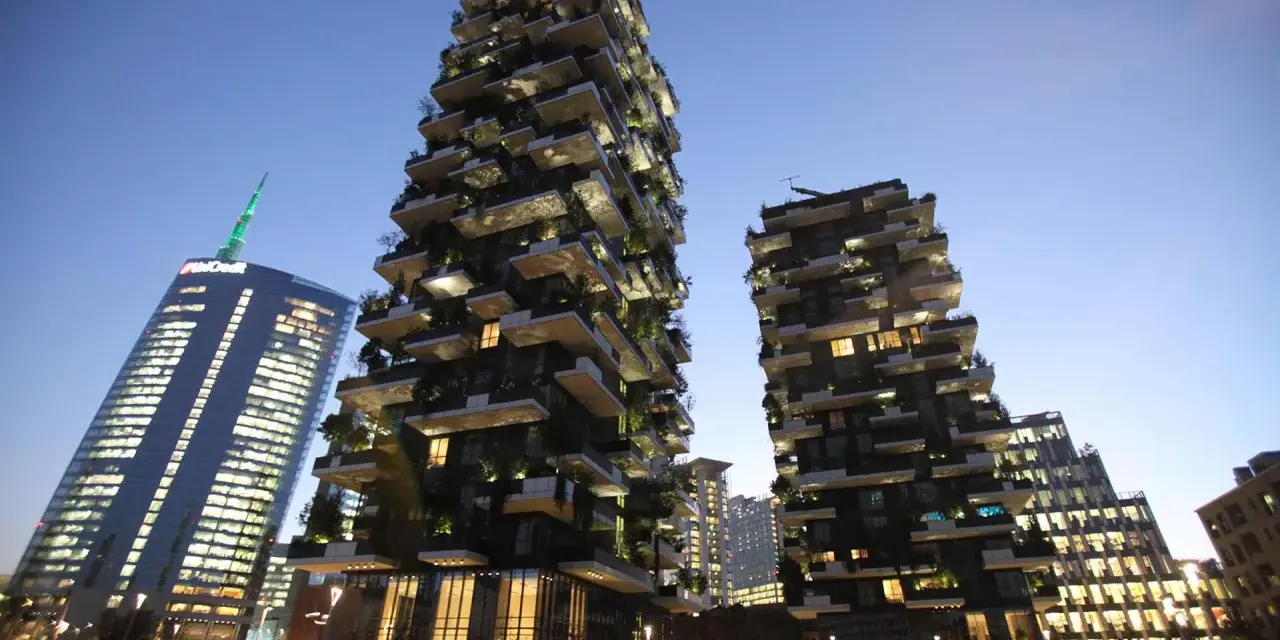 Il Bosco Verticale di Milano, con i suoi grattacieli ricoperti di alberi e piante, si staglia contro il cielo serale.