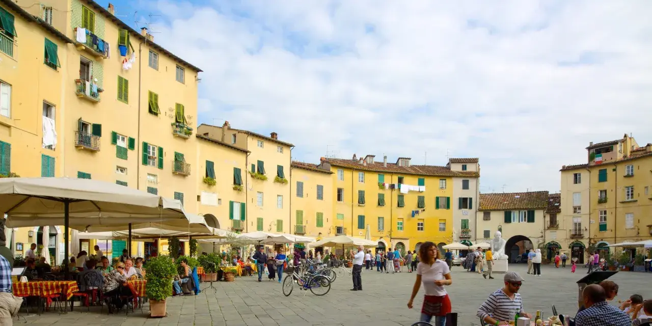 Passeggiata nella storica piazza anfiteatro di Lucca, con i suoi palazzi gialli e i tavolini all'aperto.