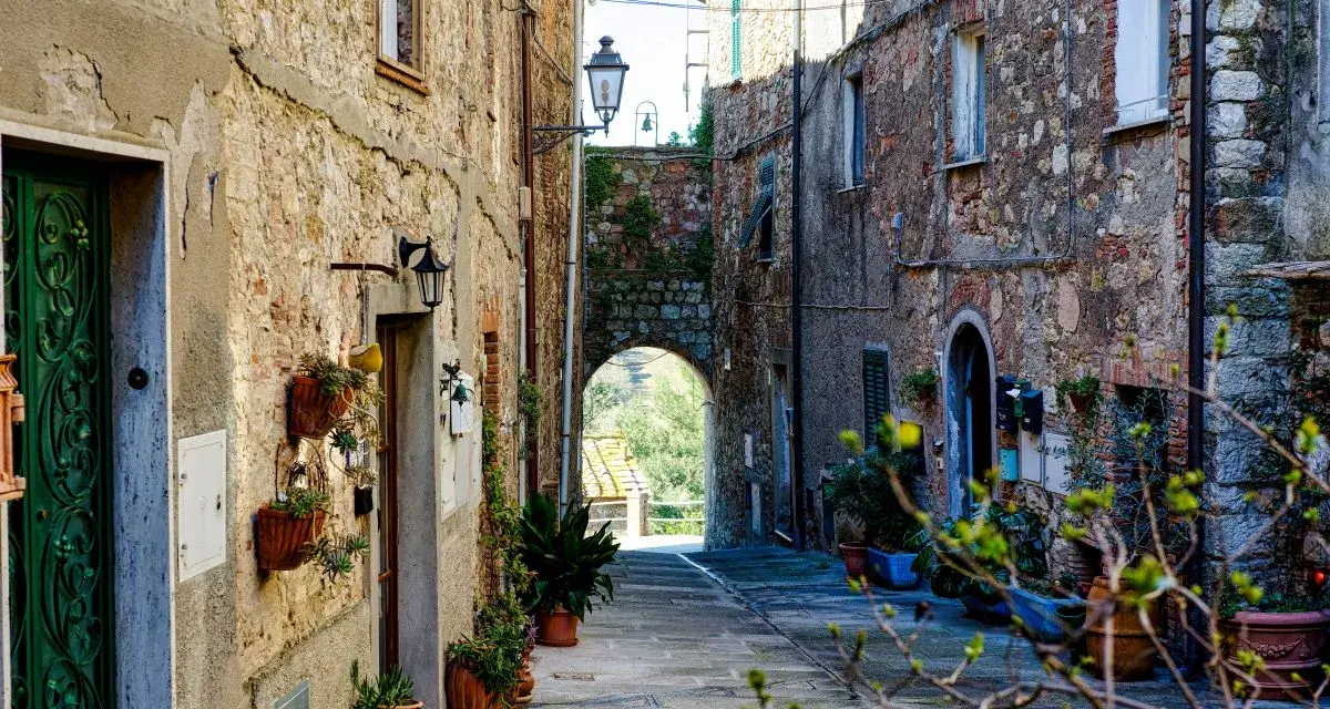Un vicolo suggestivo a Monteverdi Marittimo, con case in pietra, piante in vaso e un arco che si apre su un paesaggio verde.