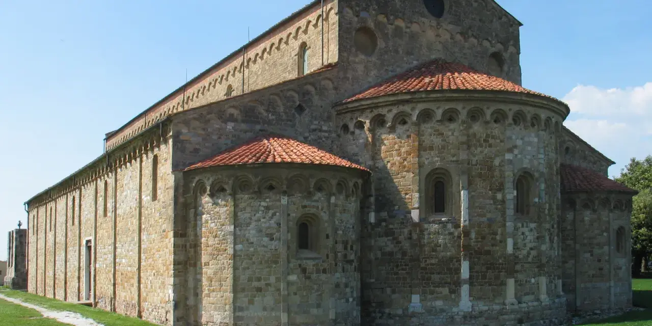 Antica basilica romanica di San Piero a Grado, con absidi semicircolari e tetto in cotto, immersa nel verde.