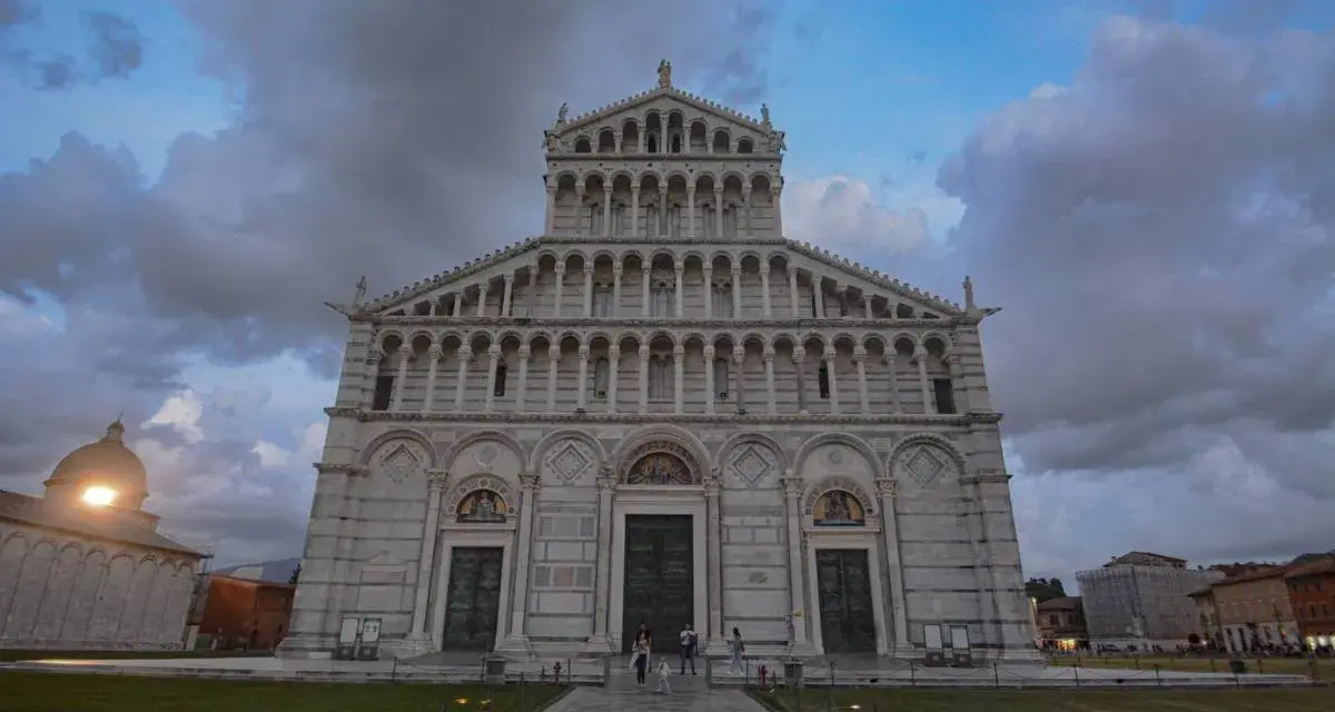 La maestosa **cathédrale de Pise** si erge sotto un cielo nuvoloso, con la sua facciata ricca di arcate e decorazioni.