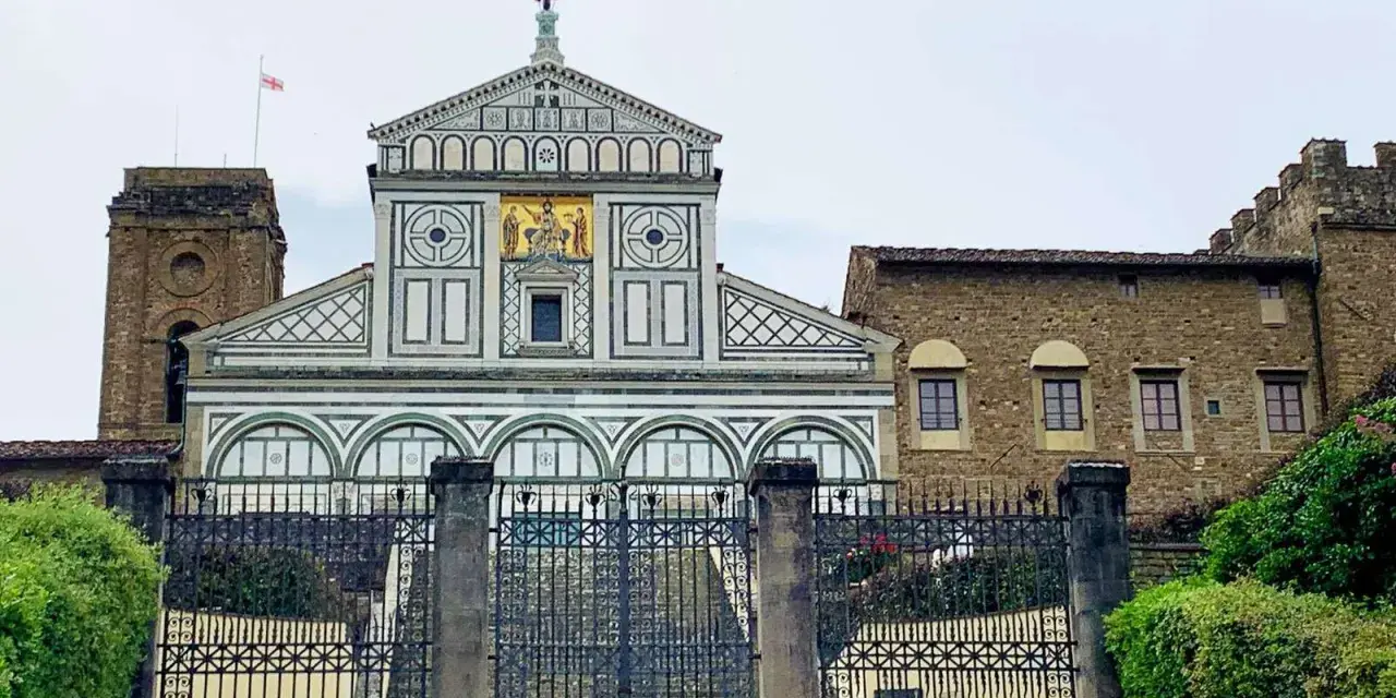 La facciata marmorea di San Miniato al Monte domina la vista, con un cancello in ferro battuto che precede la scalinata.