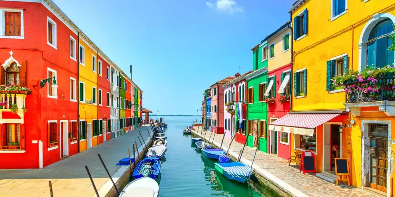 Coloratissime case affacciate su un canale, con barche ormeggiate. Un'immagine che invita a scoprire le splendide venezia isole da visitare.