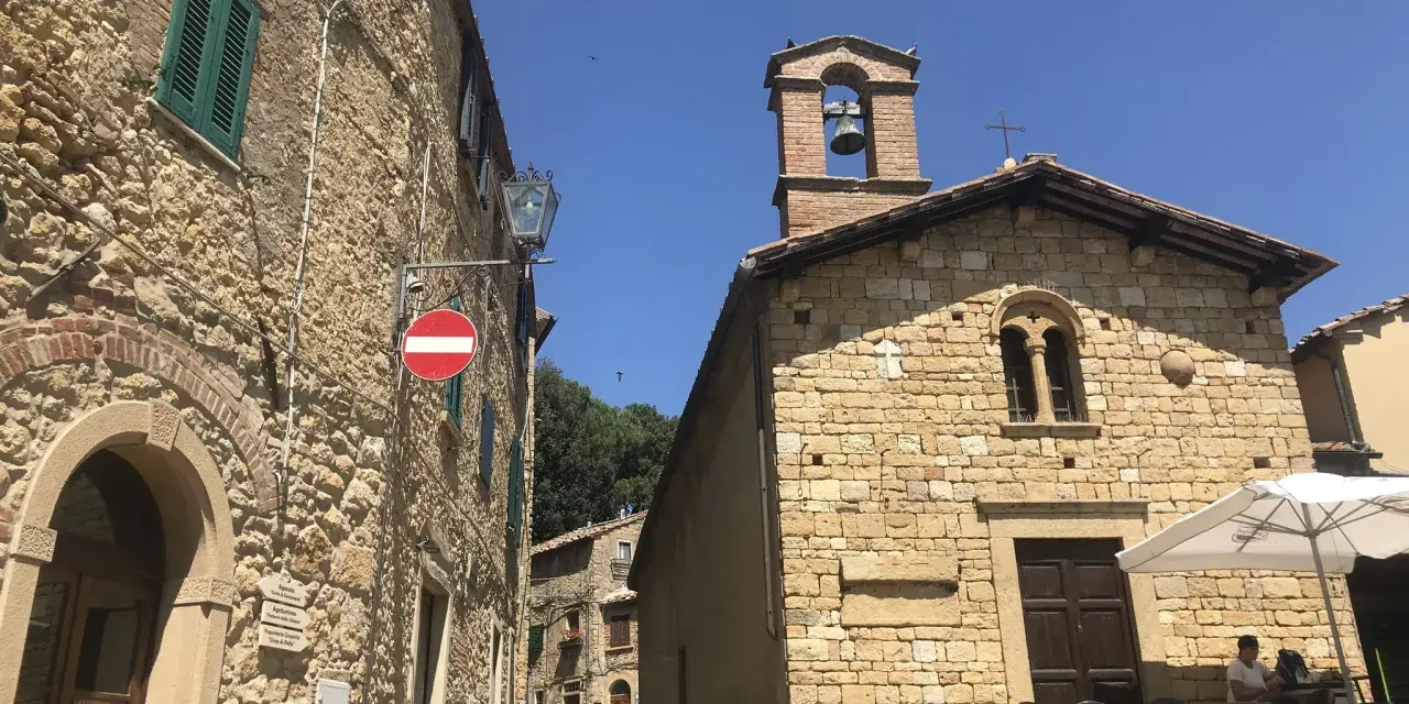 Un vicolo a Casale Marittimo, Pisa, con edifici in pietra, una chiesa con campanile e un tavolino all'aperto.