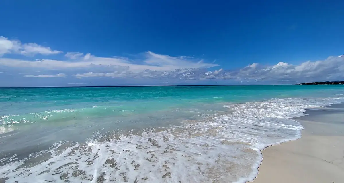 Onde turchesi lambiscono le spiagge bianche di Marina di Cecina, sotto un cielo azzurro con nuvole sparse.