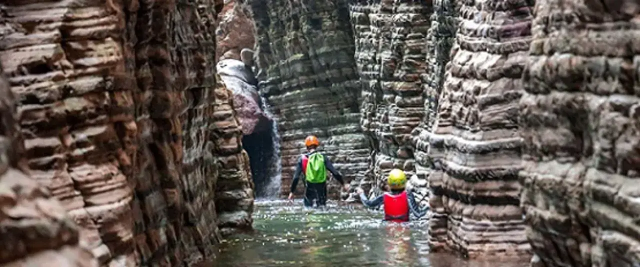 Esploratori in un canyon, tra rocce stratificate e acqua limpida, attraversano i **stretti di giaredo**.