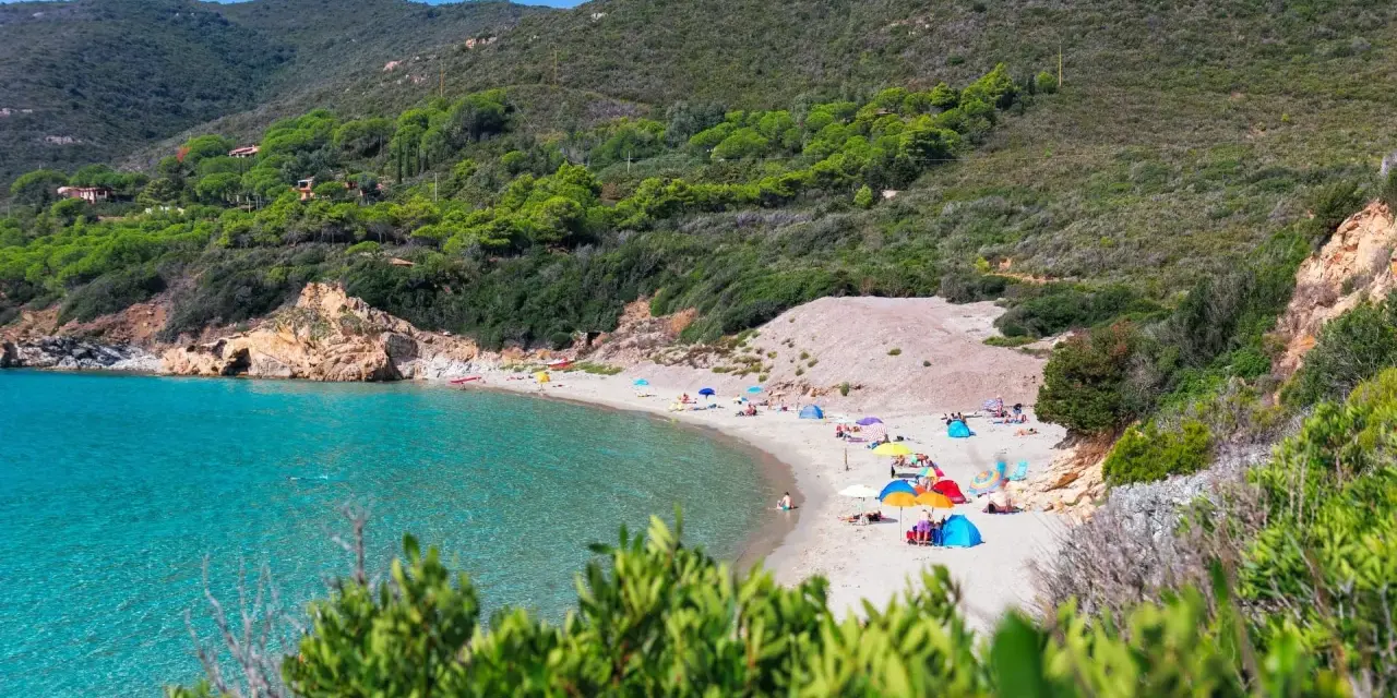 Una baia con acque cristalline e **spiagge** dell'Isola d'Elba, con ombrelloni colorati e gente che si rilassa sulla sabbia dorata.