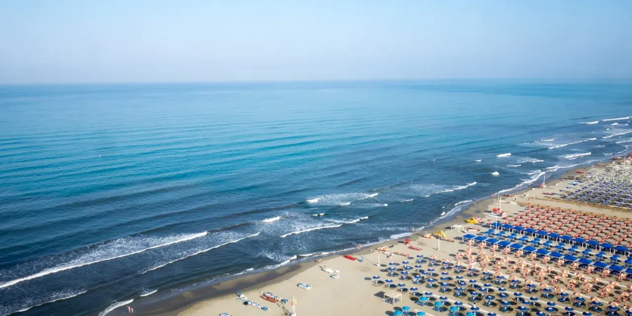 Ampia spiaggia libera al Lido di Camaiore, con file ordinate di ombrelloni e lettini che si estendono verso il mare azzurro.