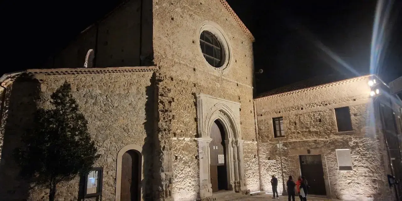 La chiesa di San Giovanni in Fiore illuminata di notte, con la sua facciata in pietra e il rosone circolare.