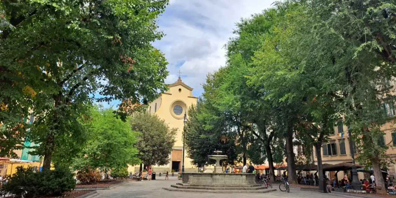 Piazza Santo Spirito a Firenze, con la chiesa sullo sfondo, una fontana al centro e alberi rigogliosi che incorniciano la scena.