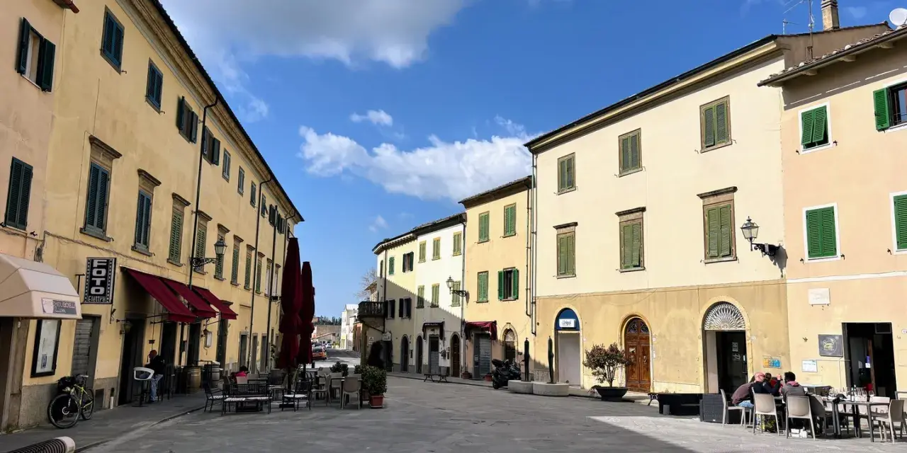 Piazza tranquilla a Pomarance, cosa vedere: edifici storici con persiane verdi, tavolini all'aperto di un bar.