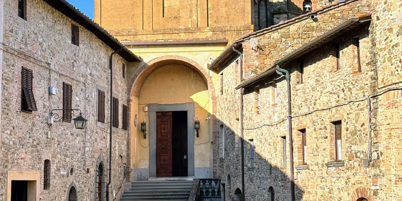 Chianni cosa vedere: un vicolo con case in pietra, una chiesa con un grande portale in legno e una scalinata.
