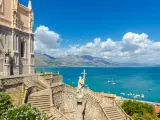 La chiesa domina il mare azzurro della Riviera di Ulisse. Scale imponenti conducono a un portale gotico, mentre barche solcano le acque.