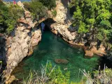 Bagni Regina Giovanna: una baia nascosta con acque cristalline, rocce scolpite e vegetazione lussureggiante. Persone si godono il sole e nuotano.