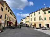 Piazza tranquilla a Pomarance, cosa vedere: edifici storici con persiane verdi, tavolini all'aperto di un bar.
