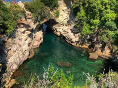 Bagni Regina Giovanna: una baia nascosta con acque cristalline, rocce scolpite e vegetazione lussureggiante. Persone si godono il sole e nuotano.