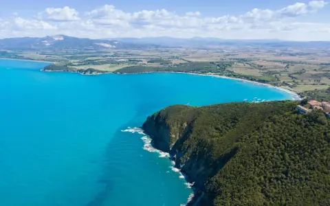 Vista aerea della costa degli Etruschi con mare azzurro, scogliere verdi e un borgo storico.