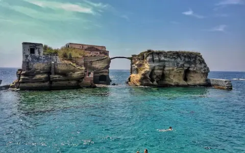 L'isola di Gaiola, con le sue rovine suggestive e il mare cristallino, accoglie bagnanti e nuotatori in una giornata di sole.