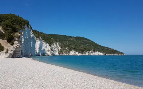 Scogliera bianca a picco sul mare turchese, con una spiaggia di ciottoli bianchi. Un angolo di paradiso, la spiaggia bianca Puglia.