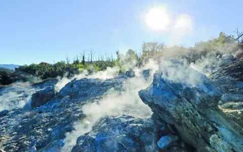 Fumarole attive nella valle del diavolo, con rocce grigie e blu avvolte dal vapore. Il sole splende nel cielo azzurro.